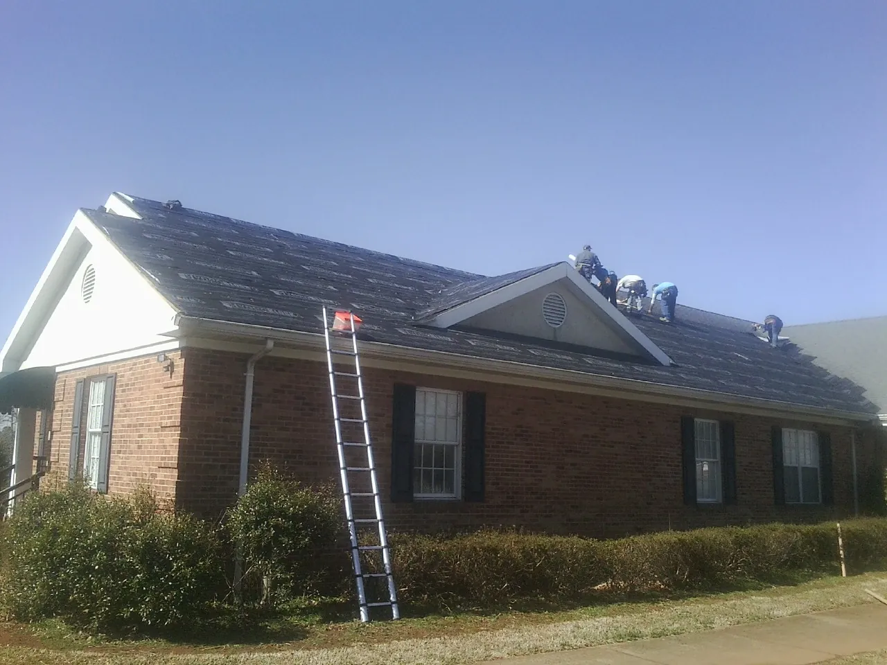 Crew tearing shingles off a brick ranch roof with a ladder set — Emergency Roof Repair work by our crew in Westlake